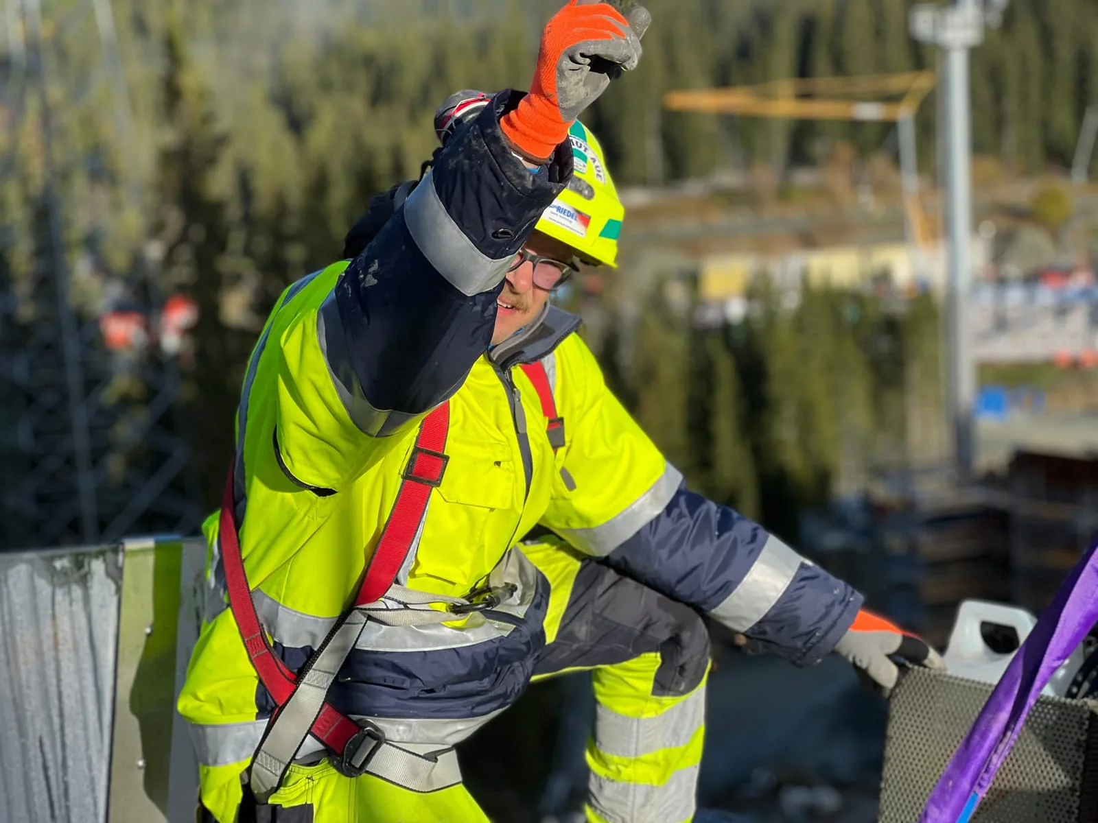 Monteur mit Auffanggurt weist den Kranführer auf der Baustelle ein