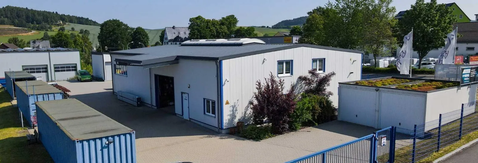 Luftaufnahme des Werksgeländes der Peter Riedel GmbH in Raschau, Fertigungshalle mit offenem Tor, Lagercontainern und Firmenfahnen